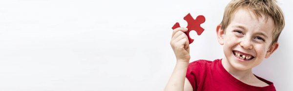 Bambino sorridente con pezzo di puzzle rosso: simbolo dell'autismo e del supporto offerto dall'olio di cannabis.